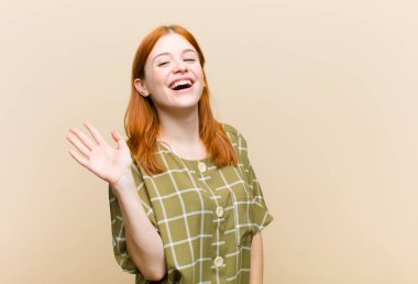 Genç kızıl saçlı güzel kadın mutlu ve neşeyle gülümsüyor, el sallıyor, seni selamlıyor ya da veda ediyor.