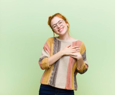 Genç, güzel, kızıl saçlı, romantik, mutlu ve aşık, neşeyle gülümseyen ve yeşil duvara yakın el ele tutuşan bir kadın.