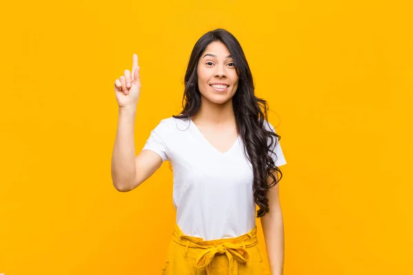 若いラテン系の女性は陽気で楽しそうに笑ってオレンジの壁にスペースをコピーするために片手で上を向いて — ストック写真