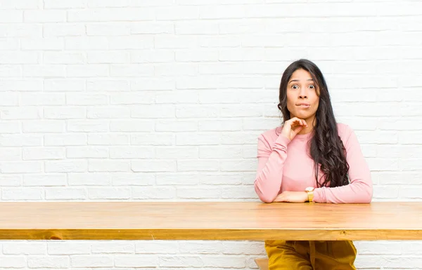 若いラテン系の女性は テーブルの前に座っている問題を解決しようとして 選択するかどうかわからず 混乱し 不確定な感じ — ストック写真