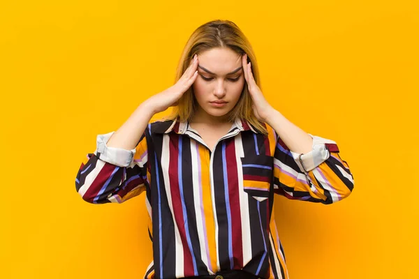 young blonde pretty woman looking stressed and frustrated, working under pressure with a headache and troubled with problems against orange wall