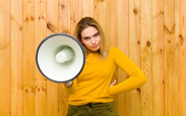 young pretty blonde woman with a megaphone against wood wall