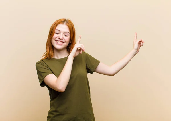 young red head pretty woman smiling happily and pointing to side and upwards with both hands showing object in copy space