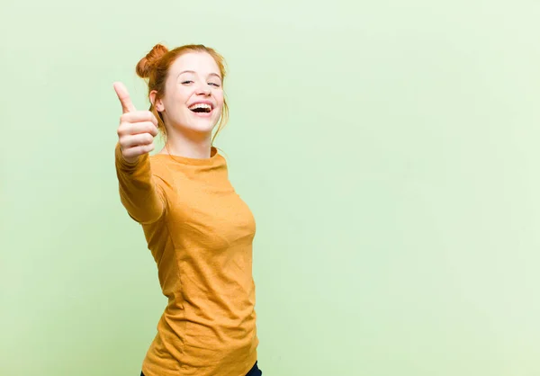 若いかなり赤い頭の女性は誇りを感じます 屈託のない 自信と幸せ 緑の壁に対して親指で積極的に笑顔 — ストック写真