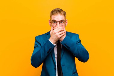 Genç, kızıl kafalı iş adamı şok olmuş, şaşırmış bir ifadeyle ağzını kapatıyor, sır saklıyor ya da turuncu arka planda 
