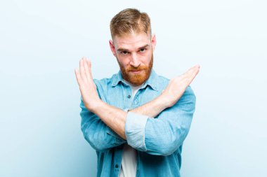 Genç kızıl saçlı adam senin bu tavırlarından rahatsız ve bıkkın görünüyor, yeter artık! Eller önde çapraz, yumuşak mavi arka planda durmanı söylüyor.