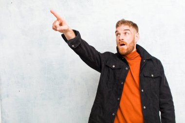 Genç kızıl saçlı adam şaşkın ve şaşırmış hissediyor, hayranlıkla yukarı bakıyor ve şaşırmış, ağzı açık bir şekilde grunge duvarına bakıyor