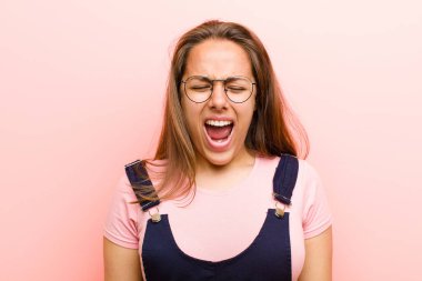 Genç bir kadın agresif bir şekilde bağırıyor, çok kızgın, hayal kırıklığına uğramış, öfkeli ya da sinirli görünüyor, pembe arka plana hayır diye bağırıyor.