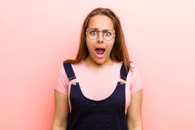Genç kadın korkmuş ve şok olmuş hissediyor, ağzı açık pembe arka plana karşı şaşkınlık içinde.