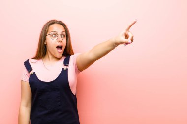 Şok olmuş ve şaşırmış hisseden genç bir kadın. Pembe arka planda hayret dolu, açık ağızlı bir bakışla yukarılara bakıyor.