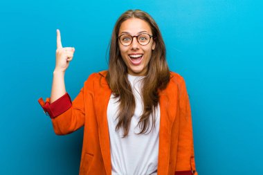 Genç bir kadın bir fikri fark ettikten sonra mutlu ve heyecanlı bir dahi gibi hissediyor, neşeli bir şekilde parmağını kaldırıyor, eureka! mavi arkaplan