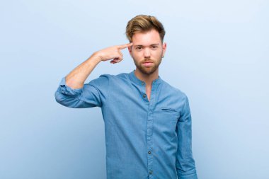 Genç işadamı kafası karışık ve şaşkın hissediyor. Deli, deli ya da mavi arka plana karşı aklını kaçırmış olduğunu gösteriyor.