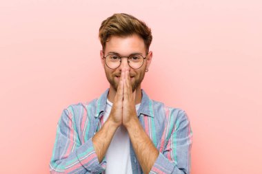 Genç adam mutlu ve heyecanlı, şaşırmış ve şaşırmış elleri ağızda, pembe arka plana karşı sevimli bir ifadeyle kıkırdıyor.