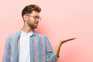 Genç adam kendini mutlu hissediyor ve gelişigüzel gülümsüyor. Elinde pembe arka plana karşı duran bir nesneye ya da konsepte bakıyor.