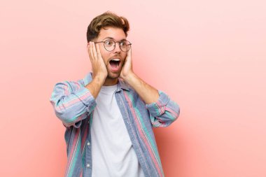 Genç adam mutlu, heyecanlı ve şaşırmış, iki eli yüzü pembe arka planda, yana bakıyor