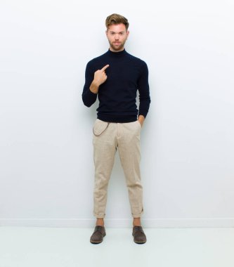 Genç tam vücut adamı gururlu, kendinden emin ve mutlu görünüyor, gülümsüyor ve kendini işaret ediyor ya da beyaz arka plana karşı bir numara işareti yapıyor.