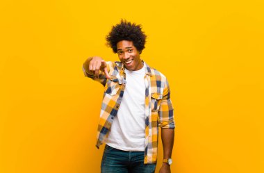 Genç siyah bir adam kameraya bakıyor. Tatmin olmuş, kendinden emin, dostane bir gülümsemeyle. Turuncu duvara karşı seni seçiyor.