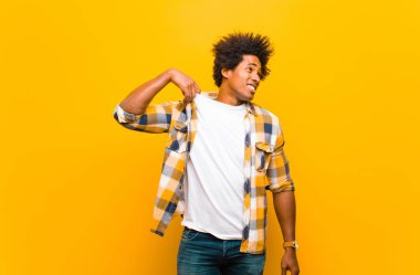 Genç siyahi adam stresli, endişeli, yorgun ve hayal kırıklığına uğramış, gömleğini çekmiş, turuncu duvara karşı sorunlu görünüyor.