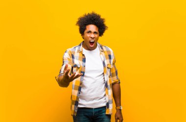 Genç siyah adam sinirli, sinirli ve hayal kırıklığına uğramış görünüyor. Turuncu duvara karşı senin neyin var? 