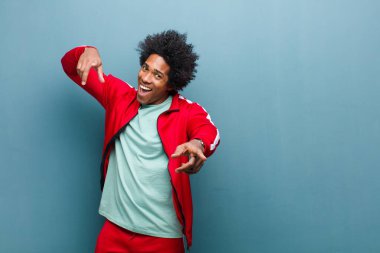 Genç siyah sporcu mutlu ve kendinden emin hissediyor, kamerayı iki eliyle gösteriyor ve gülüyor, grunge duvarına karşı seni seçiyor.