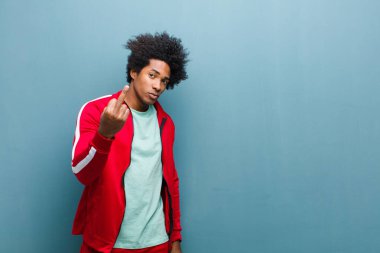 Genç siyah sporcu sinirli, sinirli, asi ve agresif orta parmağını sallayarak, grunge duvarına karşı savaşıyor.