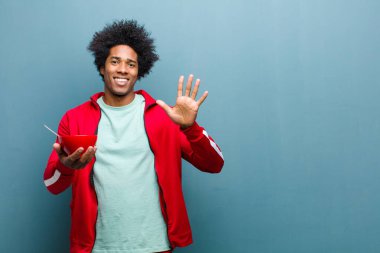 Mavi grunge duvarına karşı elinde kahvaltı kasesi olan genç siyah bir adam.