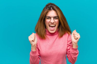 Genç ve güzel bir kadın sinirli sinirli, sinirli bakışlar ve sıkı yumruklarla bağırıyor. Mavi arka plana karşı öfkeli hissediyor.