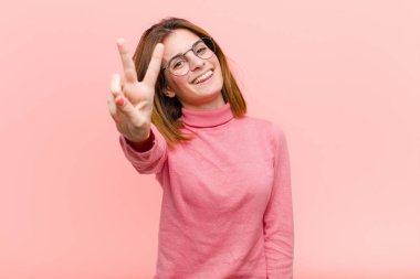 Genç, güzel bir kadın gülümsüyor ve arkadaş canlısı görünüyor. İki ya da iki numarayı gösteriyor. Elleri önde, pembe arka planda geriye doğru sayıyor.