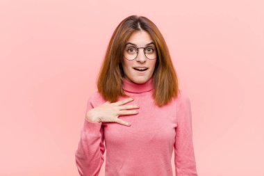 Genç, güzel bir kadın şok olmuş, şaşırmış ve şaşırmış hissediyor, elleri göğsünde ve ağzı açık, kim diyor, ben mi? Pembe arkaplan