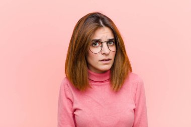 Genç ve güzel bir kadın şaşkın ve şaşkın hissediyor, aptal, şaşkın bir ifadeyle pembe arka planda beklenmedik bir şeye bakıyor.