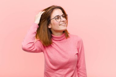 Genç ve güzel bir kadın neşeyle gülümsüyor, pembe arka plana karşı pozitif, mutlu ve kendinden emin bir bakışla göğüs göğüse tutuşuyor.