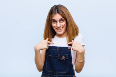 Genç, güzel bir kadın kendini mutlu, şaşırmış ve gururlu hissediyor. Heyecanlı ve şaşkın bir bakışla mavi arka plana bakıyor.