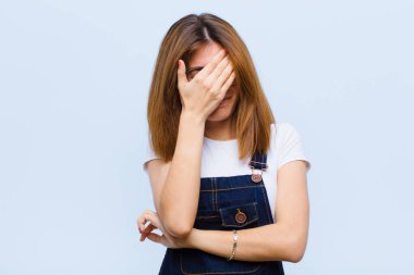 Genç, güzel bir kadın stresli, utanmış ya da üzgün görünüyor. Başı ağrıyor, yüzü mavi arka planda.