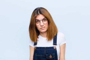 young pretty woman feeling puzzled and confused, with a dumb, stunned expression looking at something unexpected against blue background