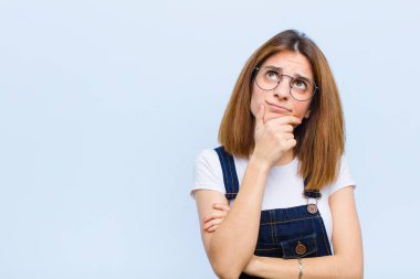Genç, güzel bir kadın düşünüyor, kuşkulu ve şaşkın hissediyor, farklı seçenekleri var, mavi arka plana karşı hangi kararı vereceğini merak ediyor.