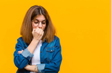 Genç, güzel bir kadın ciddi, düşünceli ve endişeli. Eli çenesine değmiş, sarı arka planda.