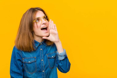 Genç ve güzel bir kadın profili görünüşü, mutlu ve heyecanlı görünüyor, bağırıyor ve sarı arka plandaki boşluğu kopyalamak için çağırıyor.