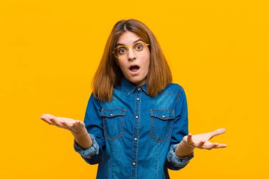 Genç ve güzel bir kadın son derece şok ve şaşırmış, endişeli ve paniklemiş hissediyor, sarı arka planda stresli ve dehşete düşmüş bir bakışla