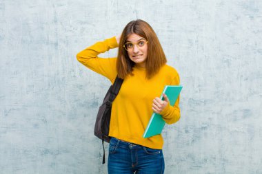 Genç bayan kendini stresli, endişeli, endişeli ya da korkmuş hissediyor, elleri başının üstünde, grunge duvar arka planına karşı yanlışlıkla panikliyor.