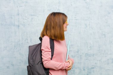 Profil görünümlü genç bir bayan, Grunge Wall arka planına bakarak, düşünme, hayal kurma ya da hayal kurma boşluğunu kopyalamaya çalışıyor.