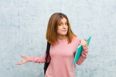 Genç bir bayan öğrenci kendini cahil ve kafası karışık hissediyor, hiçbir fikri yok, grunge duvarına bakan aptal ya da aptal bir bakışla tamamen şaşkına dönmüş.
