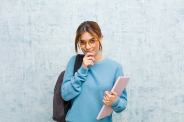Genç bayan ciddi görünüyor, kafası karışık, kararsız ve düşünceli, seçenekler arasında veya grunge duvar arka planına karşı seçimler