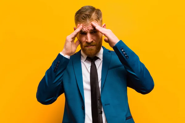 young red head businessman looking stressed and frustrated, working under pressure with a headache and troubled with problems against orange background