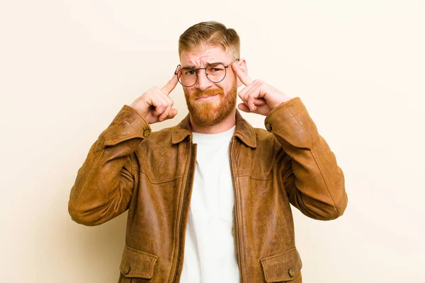 young red head man feeling confused or doubting, concentrating on an idea, thinking hard, looking to copy space on side against beige background