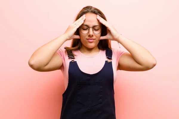 young  woman looking stressed and frustrated, working under pressure with a headache and troubled with problems against pink background