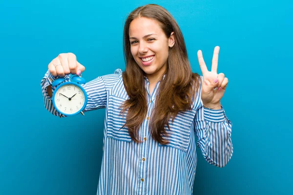 Mujer joven con despertador contra fondo azul — Foto de Stock