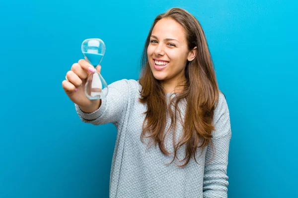 Jonge vrouw met zand timer tegen blauwe achtergrond — Stockfoto