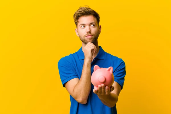 Junger Mann Mit Sparschwein Vor Orangefarbenem Hintergrund — Stockfoto