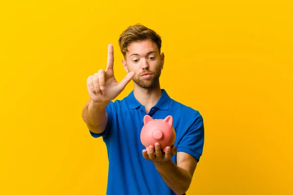 Jonge Man Met Een Spaarvarken Bank Tegen Oranje Achtergrond — Stockfoto