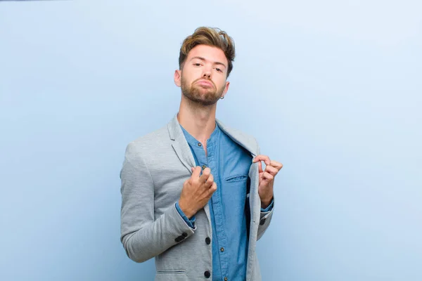 young businessman looking arrogant, successful, positive and proud, pointing to self against blue background
